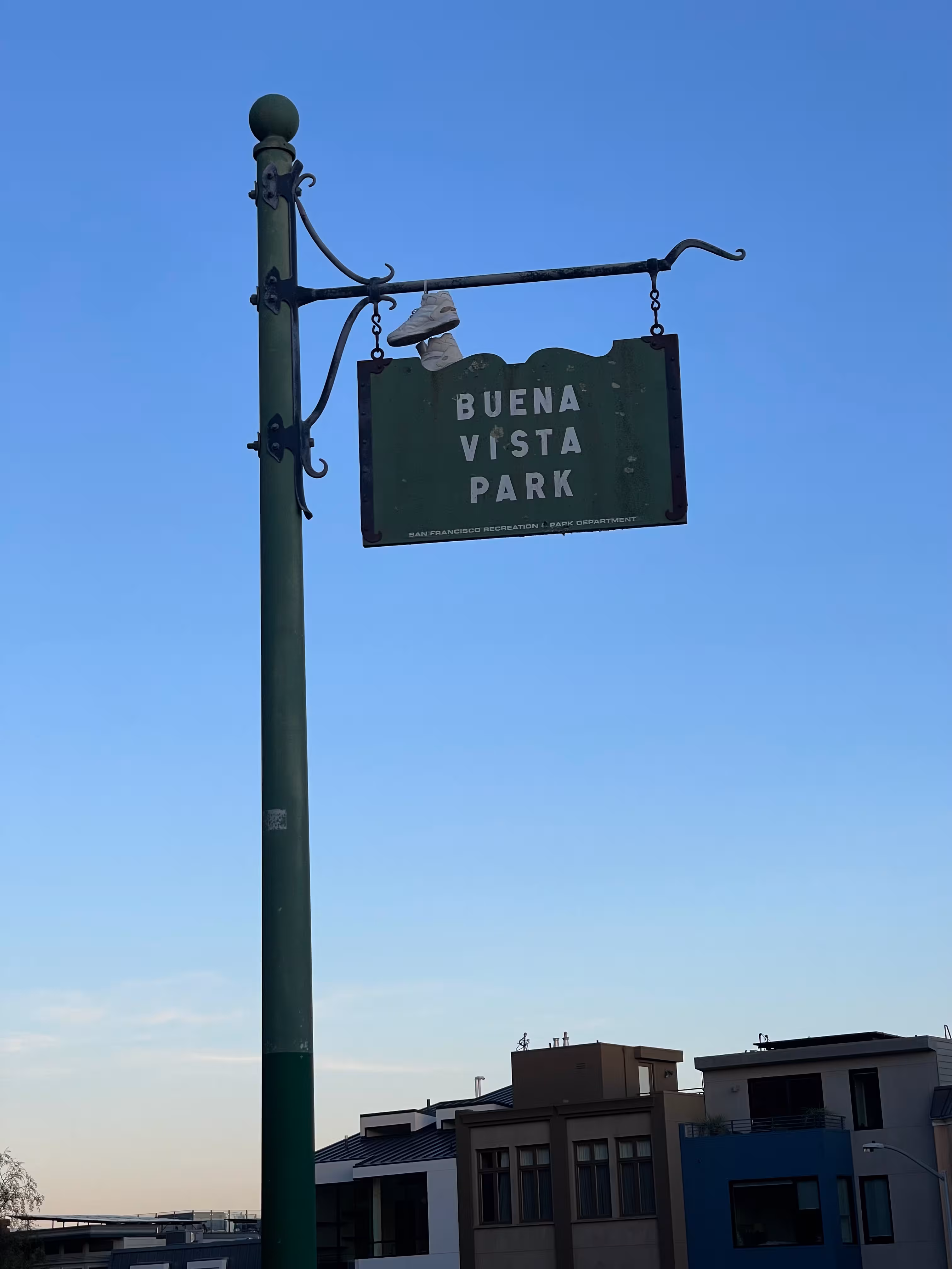 A sign that says 'Buena Vista Park' with a pair of white sneakers thrown on top of it.